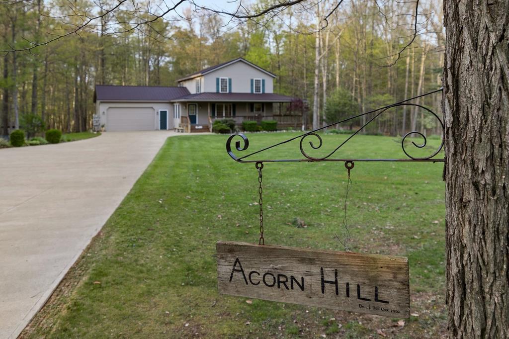 view of front of house with covered porch, driveway, a garage, a view of trees, and a front lawn