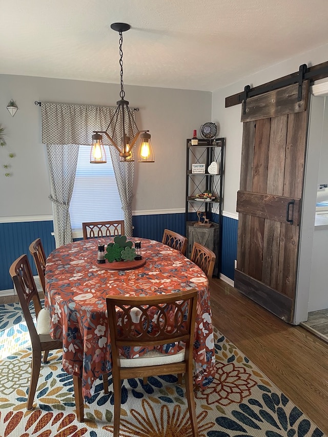 dining area featuring a wainscoted wall, a barn door, and wood finished floors