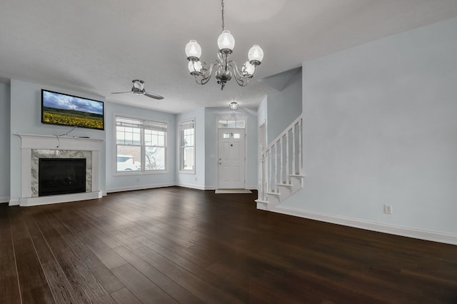 unfurnished living room featuring a high end fireplace, ceiling fan with notable chandelier, and dark wood-type flooring