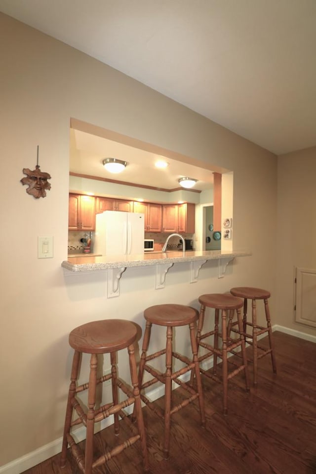 10411 River Rd, Huron, OH 44839 - kitchen with freestanding refrigerator, dark wood-type flooring, a kitchen bar, a peninsula, and brown cabinets