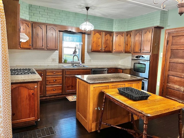 kitchen with brown cabinetry, a sink, decorative backsplash, and stainless steel appliances