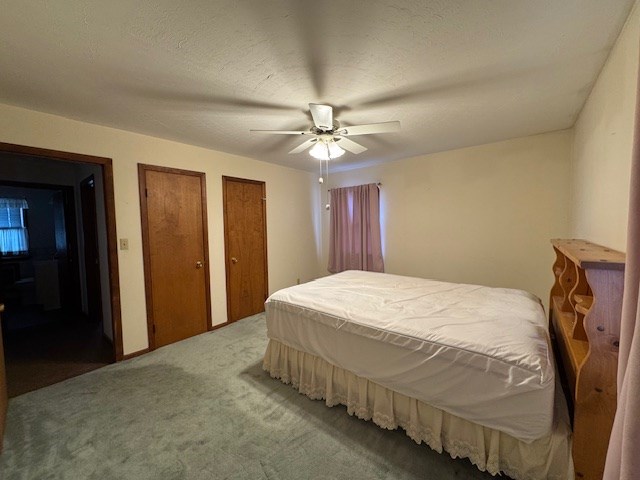 carpeted bedroom featuring ceiling fan, a textured ceiling, and multiple closets