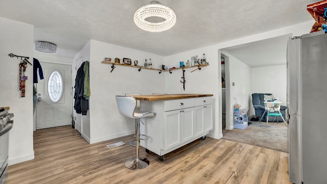 entryway with a chandelier, a textured ceiling, light wood-type flooring, and bar area