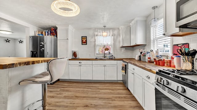 kitchen with wood counters, stainless steel appliances, pendant lighting, a notable chandelier, and white cabinetry