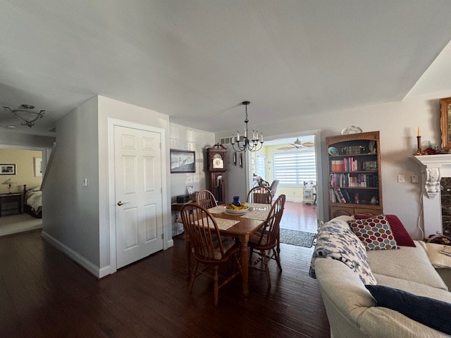 dining room with dark hardwood / wood-style flooring, ceiling fan with notable chandelier, and a fireplace