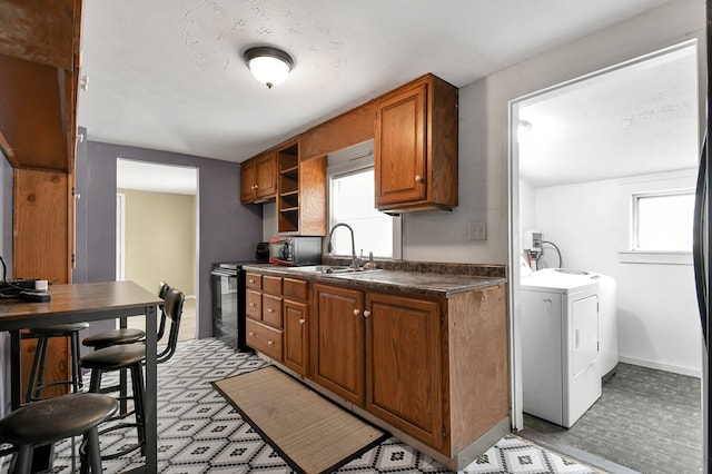 kitchen with black / electric stove, a sink, brown cabinets, washer / clothes dryer, and dark countertops