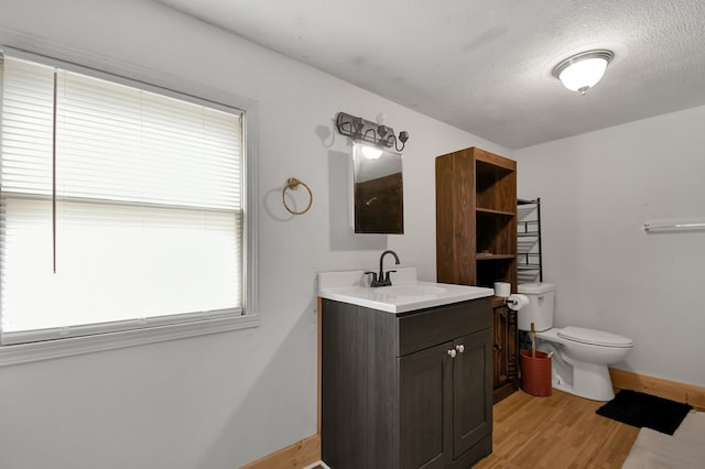 bathroom with toilet, a textured ceiling, vanity, wood finished floors, and baseboards