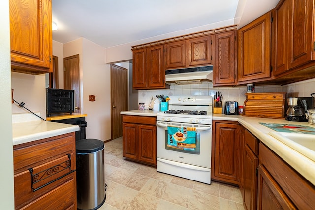7326 State Route 19 Unit 47-48, Mount Gilead, OH 43338 - kitchen with white gas range oven, under cabinet range hood, brown cabinetry, light countertops, and backsplash