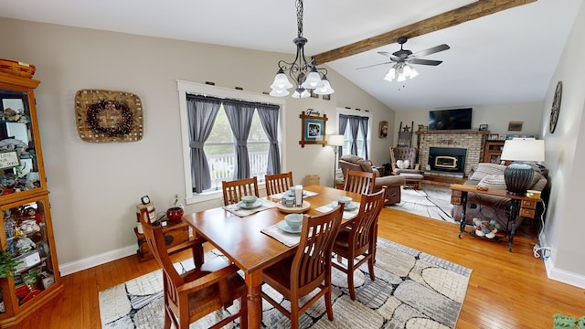 dining area featuring a fireplace, ceiling fan with notable chandelier, light hardwood / wood-style floors, and lofted ceiling with beams