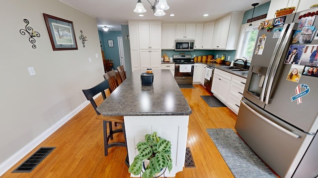 kitchen featuring a center island, a kitchen bar, white cabinets, pendant lighting, and stainless steel appliances