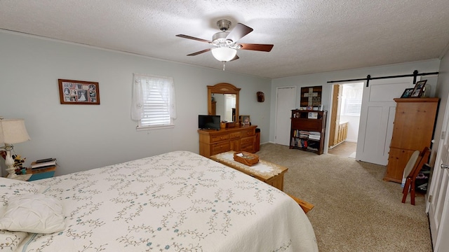 bedroom featuring a textured ceiling, a barn door, carpet, ceiling fan, and connected bathroom