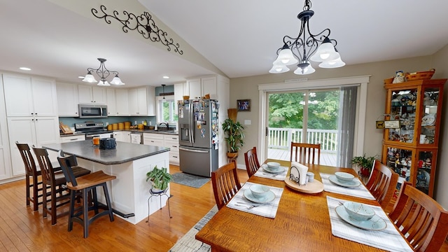 dining space with a notable chandelier, light hardwood / wood-style flooring, lofted ceiling, and sink