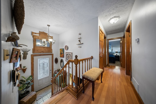 entryway featuring light wood-type flooring, a chandelier, and a textured ceiling