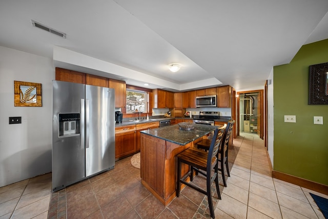 kitchen featuring appliances with stainless steel finishes, a center island, dark stone counters, sink, and a breakfast bar