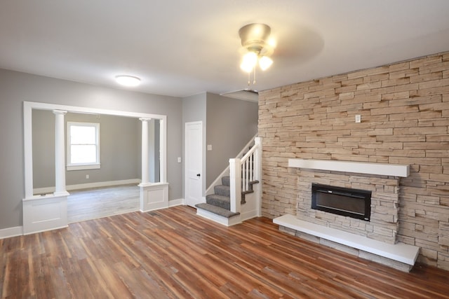 unfurnished living room featuring a stone fireplace, baseboards, stairs, and wood finished floors
