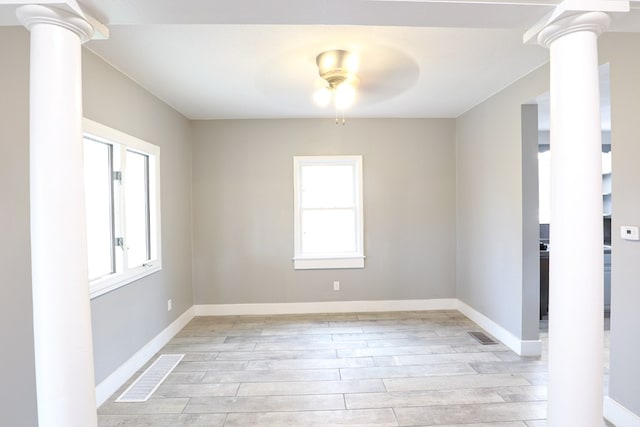 spare room featuring light wood-style flooring, a ceiling fan, visible vents, and decorative columns