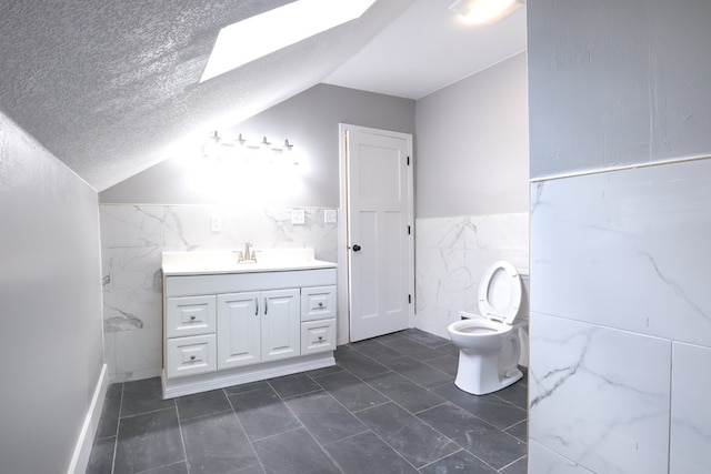 bathroom featuring tile walls, a textured ceiling, toilet, vanity, and lofted ceiling with skylight