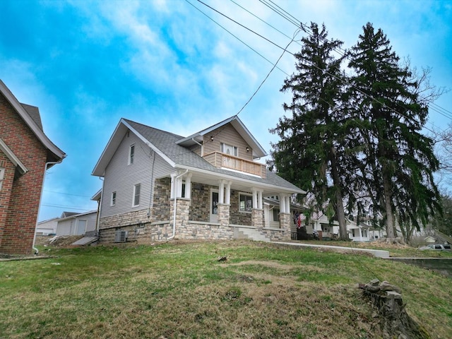 view of front of property with a balcony, stone siding, a front lawn, cooling unit, and a porch
