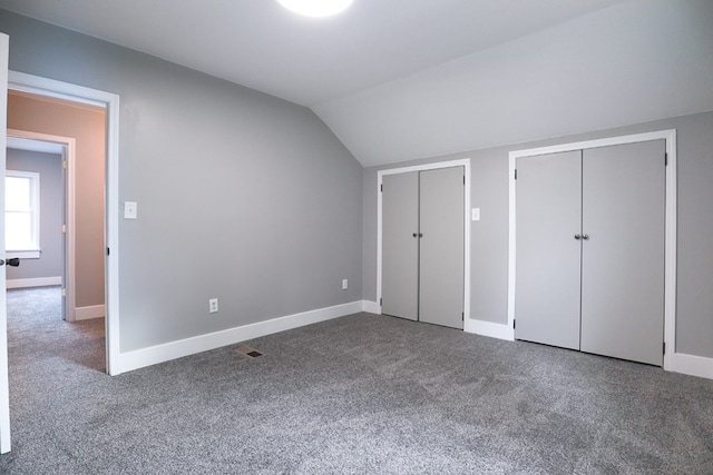 unfurnished bedroom with baseboards, lofted ceiling, two closets, and carpet flooring
