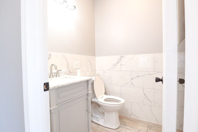 bathroom featuring a wainscoted wall, tile walls, toilet, and vanity