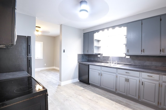 kitchen featuring baseboards, a sink, light wood-type flooring, black appliances, and backsplash