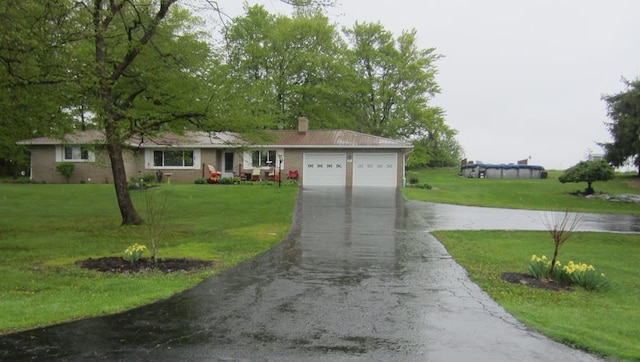 ranch-style home with a front lawn, a chimney, a garage, and aphalt driveway