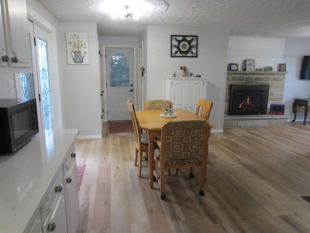 dining area featuring light wood finished floors, a textured ceiling, baseboards, and a stone fireplace