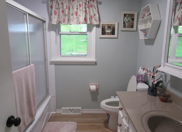 bathroom featuring toilet, bath / shower combo with glass door, visible vents, vanity, and wood finished floors