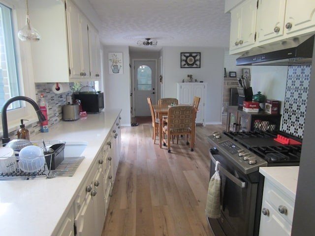 kitchen featuring under cabinet range hood, stainless steel gas range, white cabinetry, light wood-style floors, and light countertops