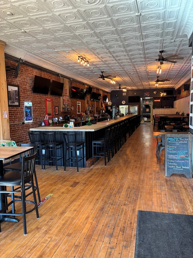 bar featuring a dry bar, wood-type flooring, an ornate ceiling, and brick wall