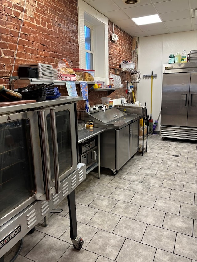 kitchen featuring stainless steel built in refrigerator, a drop ceiling, brick wall, and light tile patterned floors