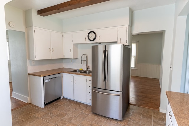 kitchen with beamed ceiling, appliances with stainless steel finishes, white cabinetry, and sink