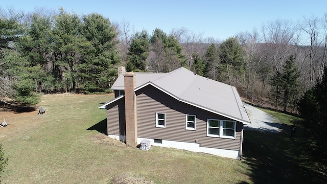 view of home's exterior with a yard, metal roof, a wooded view, and a chimney