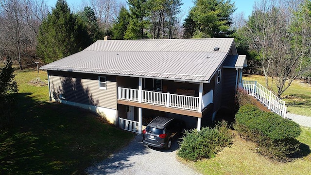 rear view of property with a chimney, metal roof, a lawn, and gravel driveway