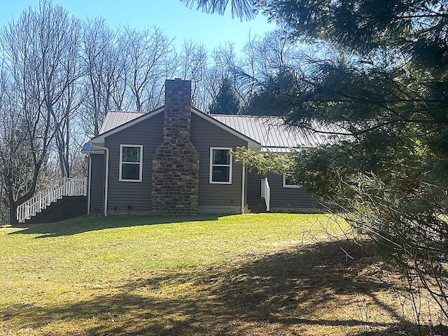view of home's exterior featuring a chimney, metal roof, a standing seam roof, and a lawn