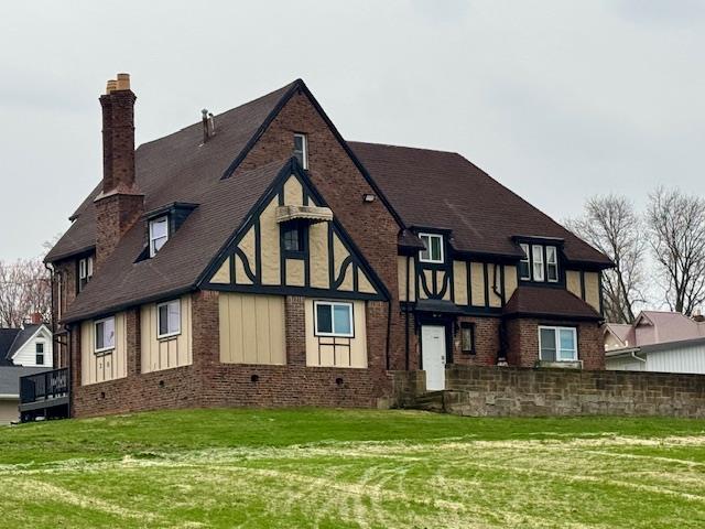 exterior space featuring brick siding, a shingled roof, a yard, and a chimney