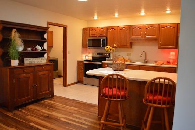 kitchen with a breakfast bar area, sink, stainless steel appliances, and light wood-type flooring