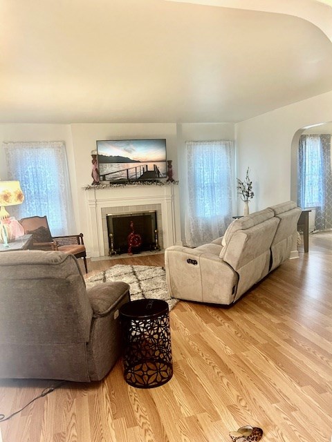 living room with arched walkways, wood finished floors, and a tile fireplace