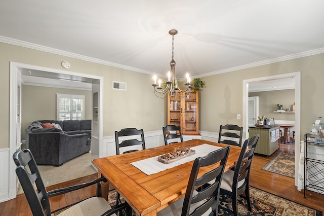 dining space with ornamental molding, wood-type flooring, and a chandelier