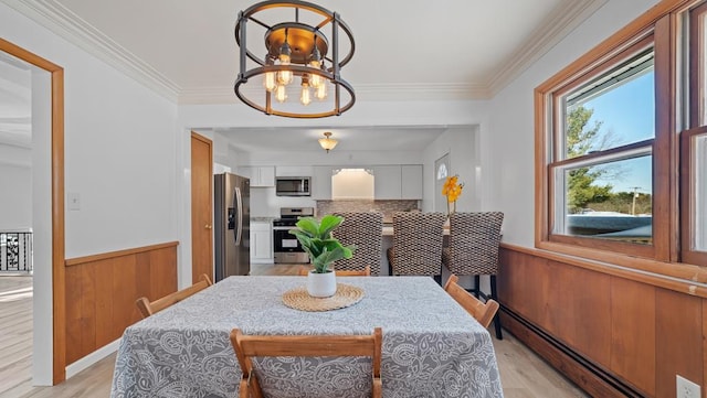 dining area with crown molding, a baseboard heating unit, an inviting chandelier, light hardwood / wood-style floors, and wood walls