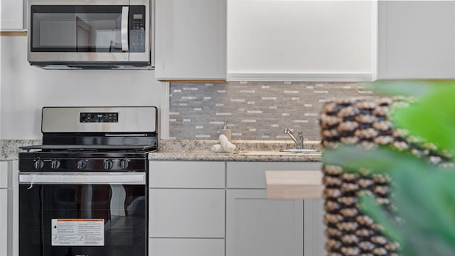 kitchen featuring tasteful backsplash, light stone countertops, white cabinets, and appliances with stainless steel finishes