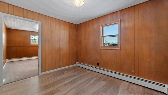 empty room featuring light hardwood / wood-style flooring, a baseboard heating unit, and wood walls