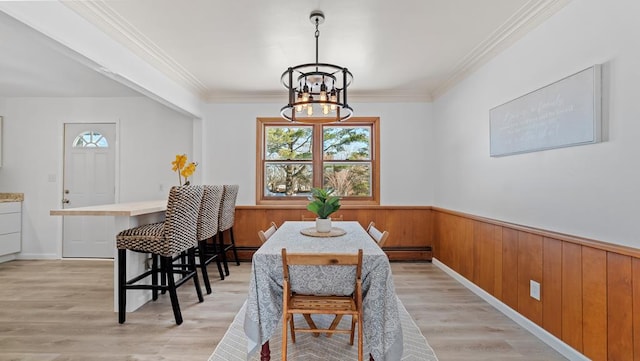 dining area featuring ornamental molding, wooden walls, a baseboard radiator, and a notable chandelier