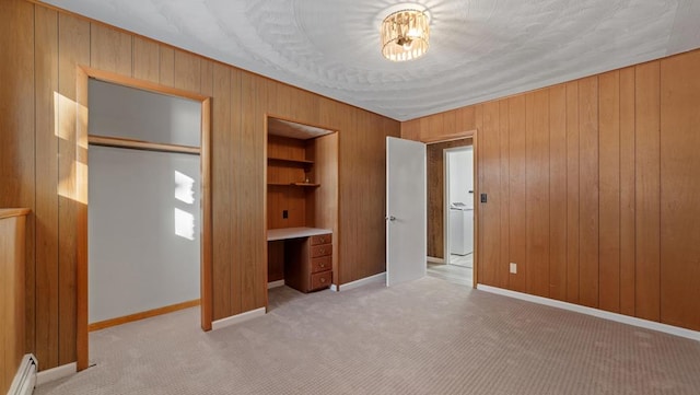 unfurnished bedroom with a baseboard heating unit, wood walls, light carpet, a closet, and built in desk