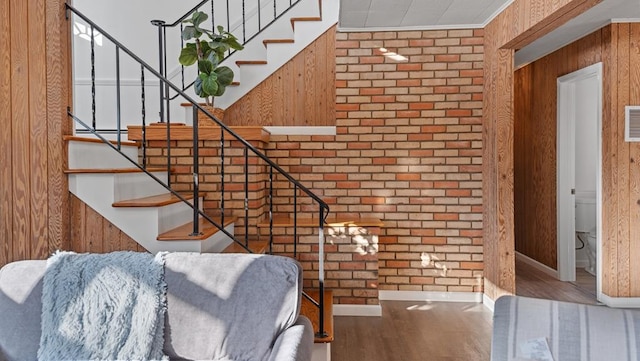 stairway with hardwood / wood-style floors, crown molding, and brick wall