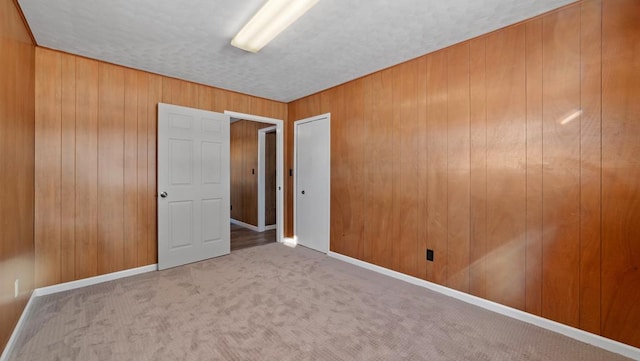 carpeted spare room with a textured ceiling and wooden walls