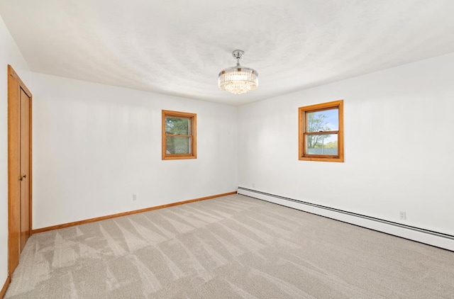 carpeted empty room featuring baseboard heating and an inviting chandelier