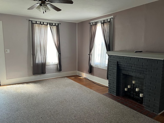 unfurnished living room with dark colored carpet, ceiling fan, a healthy amount of sunlight, and a fireplace