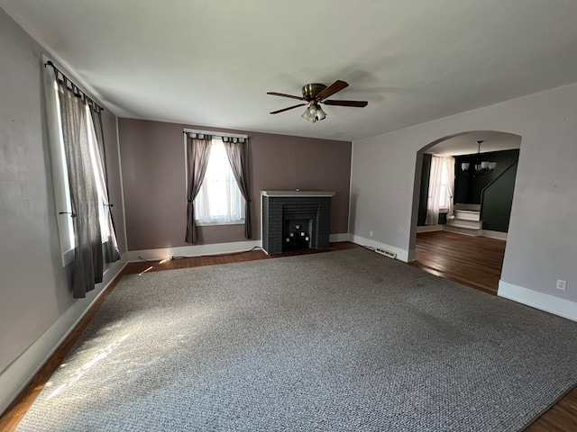 unfurnished living room featuring ceiling fan with notable chandelier, dark wood-type flooring, and a brick fireplace