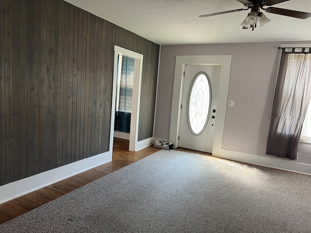 foyer entrance with ceiling fan, wood walls, and wood-type flooring